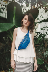 Fototapeta na wymiar A beautiful young woman on a background of tropical plants travels the world. Leather Sling Purse Bum Bag.