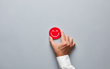 Businessman hand holding a red badge with a smiling face icon. Customer satisfaction or positive...