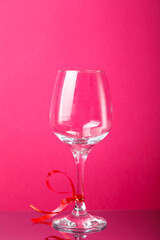 Champagne glass with red ribbon on a pink background.