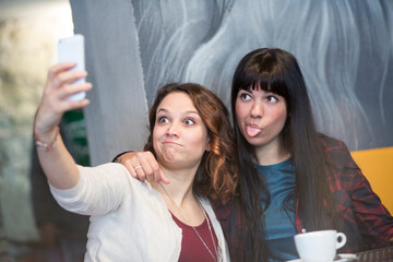 amiche si divertono a farsi un selfie con il cellulare in un locale sedute nei divanetti di fronte...