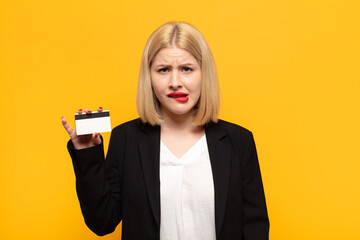 blonde woman looking puzzled and confused, biting lip with a nervous gesture, not knowing the...