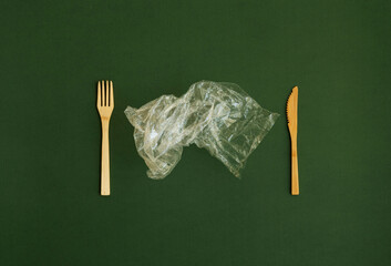 Crumpled plastic polyethylene bag with a bamboo fork and knife on a green background. Contamination...
