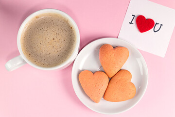 Homemade heart-shaped cookies, cup of coffee and a note with the words I love you on pastel pink color. Valentine's Day breakfast. Valentine's day concept.