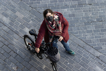 A woman looking up while holding her bicycle and wearing a face mask