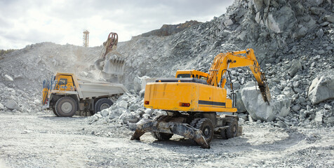 Hydraulic breaker, close-up, working in a stone quarry, with heavy mining dump truck during of loading in the background, panorama. © esalienko