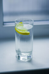 A glass of water with a slice of lemon stands on a white windowsill by the window