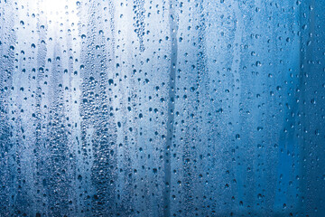 A small raindrop rests on the glass after rain. Raindrops On The Glass. Raindrops on the window. Blue tone. Abstract background.