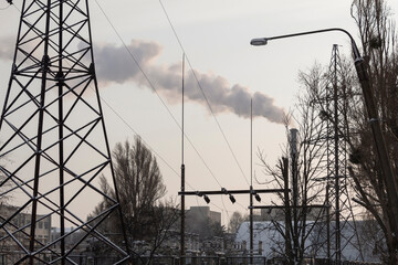 Industrial landscape. High voltage pole, wires, trees. A smoking pipe is visible in the distance.