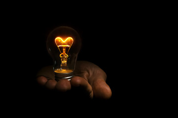 incandescent heart shaped light bulb in hand on black background for valentine's day