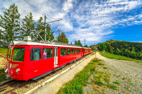 Rigi kulm, Switzerland - Aug 25, 2020: people in a popular sightseeing train travels on cogwheel railway in green meadows on Mt. Rigi. Rigi Kulm summit and telecommunications tower on background.