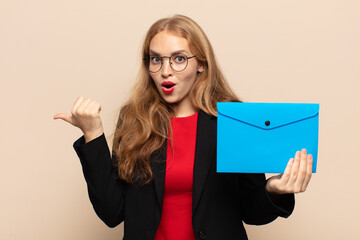 blonde woman looking astonished in disbelief, pointing at object on the side and saying wow,...