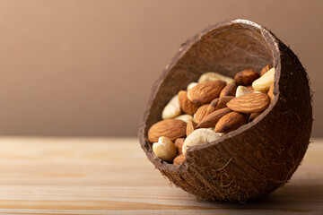 Mix of almonds, cashew nuts in coconut bowl on brown background close up. Vegan protein source