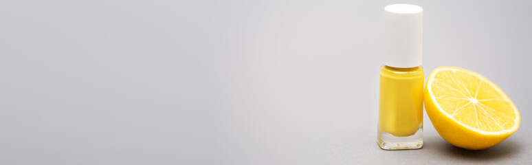 bottle with yellow nail polish and half of lemon on grey background, banner