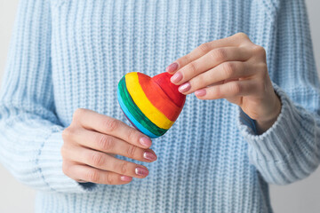 A girl in a blue sweater holds a multicolored heart in her hands, the concept of lgbt friendly