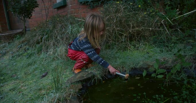 A preschooler is breaking the ice on top of a pond in the garden on a winter day