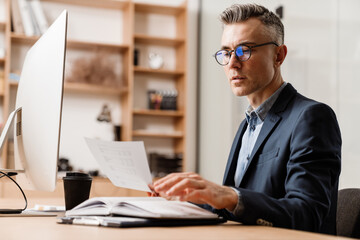 Fototapeta premium Serious grey man working with computer and planner in office