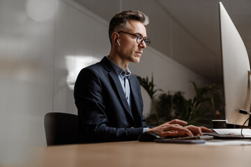 Concentrated grey man in eyeglasses working with computer at office
