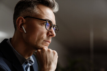 Concentrated grey man in wireless earphones working at office