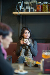 ragazza mora con gli occhi verdi e un caldo maglione  si guarda con aria affranta mentre prende una tisana calda in un bar 