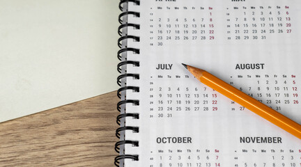 Top view of clean white paper blank, pencil and spiral calendar on wooden table background.