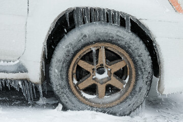 Ice buildup and icicles on a car and close-up of a frozen wheel