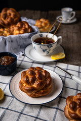 Breakfast with knot buns, orange jam and  black tea with lemon in white and blue dishes on wooden table. 