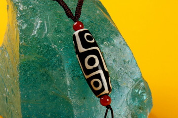 Tibetan 9 Eyes Dzi Beads necklace on green quartz crystal, yellow background.Tibet Antique Buddhist...