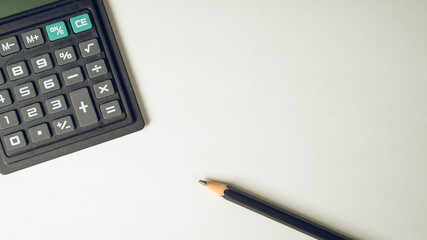 Close-up of black pencil and calculator on empty white paper blank. Top view.