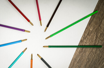 Group of different colors pivots of pens lie on empty white paper blank. Wooden table background. Top view.