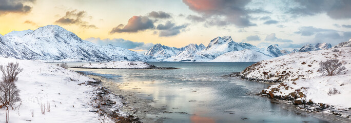 Stunning morning view of Torsfjorden fjord with cracked ice and snowy mountain peaks at background.