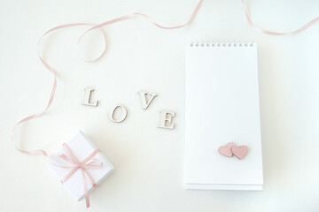 On a gentle light background gift box, notebook with free space and hearts, word love. Flat lay, top view. Lovely romantic background, great for Valentine's Day, Mother's Day, wallpapers.