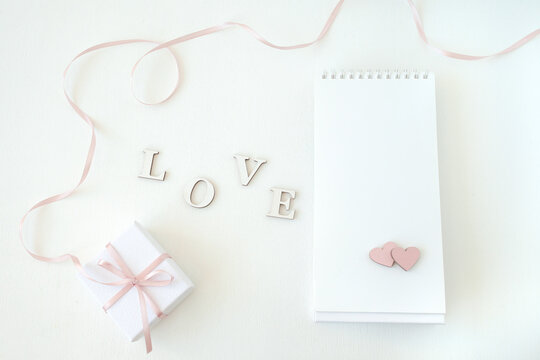 On a gentle light background gift box, notebook with free space and hearts, word love. Flat lay, top view. Lovely romantic background, great for Valentine's Day, Mother's Day, wallpapers.