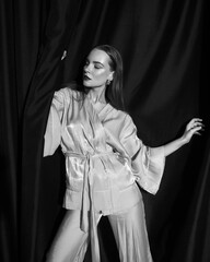 Elegant red head woman in beige kimono suit. Pretty beautiful girl standing, posing, holding black curtains in her hands and playing with them. Fashion studio portrait