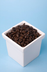 Studio photo of a white pot filled with fresh coffee beans. Isolated on light blue background. Selective focus on object.