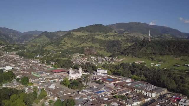Drone shot flying over the main town square in Silvia, Colombia. The drone is flying backwards to reveal more of the village.