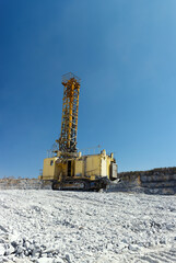 Mining drilling rig in a limestone quarry on the background of blue sky, vertical panorama. Mining machinery.