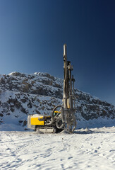 Modern mining drilling rig in a limestone open-cast mine on the background of rock wall and blue sky, vertical panorama. Mining machinery.