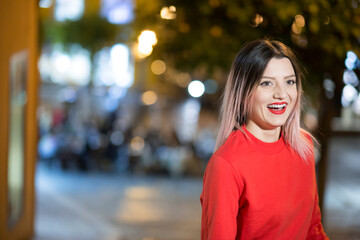 Bella ragazza bionda con maglione rosso sorride divertita in contesto urbano