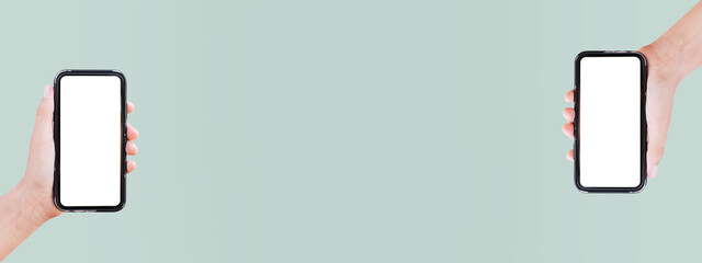 Close-up of two smartphones in hands on panoramic background of pastel green color with mid copy...