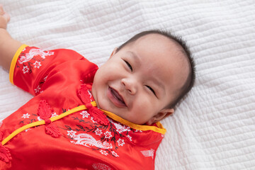 Asian cute baby boy Chinese Cheongsam costume toddler lie down on bed at home smiling laughing good humored, infant Chinese curiosity boy kid looking something, Happy Chinese New Year concept