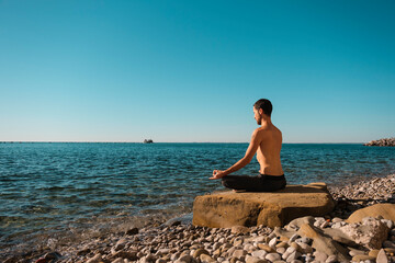 Attractive young man practicing yoga meditation and breathwork outdoors by the sea
