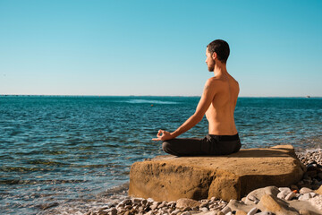 Attractive young man practicing yoga meditation and breathwork outdoors by the sea