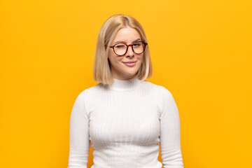 blonde woman looking happy and friendly, smiling and winking an eye at you with a positive attitude