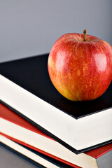 Studio photo of a red apple on top of a pile of books. Isolated on grey background. Selective focus on object.