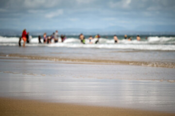Sand and ocean wave in focus, Swimmers and blue cloudy sky out of focus in the background. Nature scene. Warm sunny day