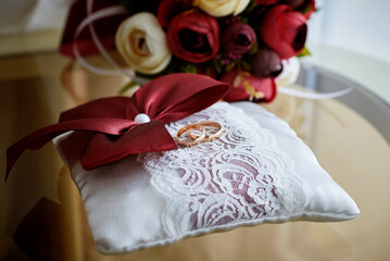 gold wedding rings on a white cushion with red bows and ornaments. close-up, macro