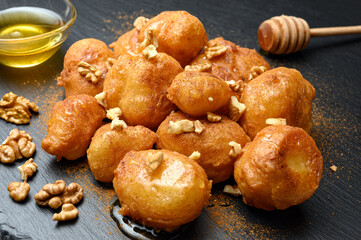 Homemade lokma served with honey, nuts and cinnamon on black dish