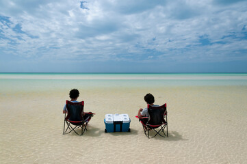 Two guys sitting in the middle of the Caribbean Ocean on chairs and iceboxes, watching the horizon. Holbox Island, Mexico. An ideal place to relax