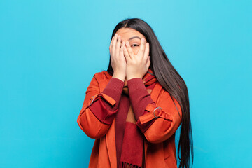 latin woman feeling scared or embarrassed, peeking or spying with eyes half-covered with hands