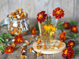 Folk medicine. A glass of medicinal tea with red flowers of marigolds-marigolds on a wooden...